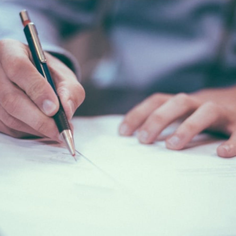 Hand holding a gold and black pen and writing on a piece of paper.